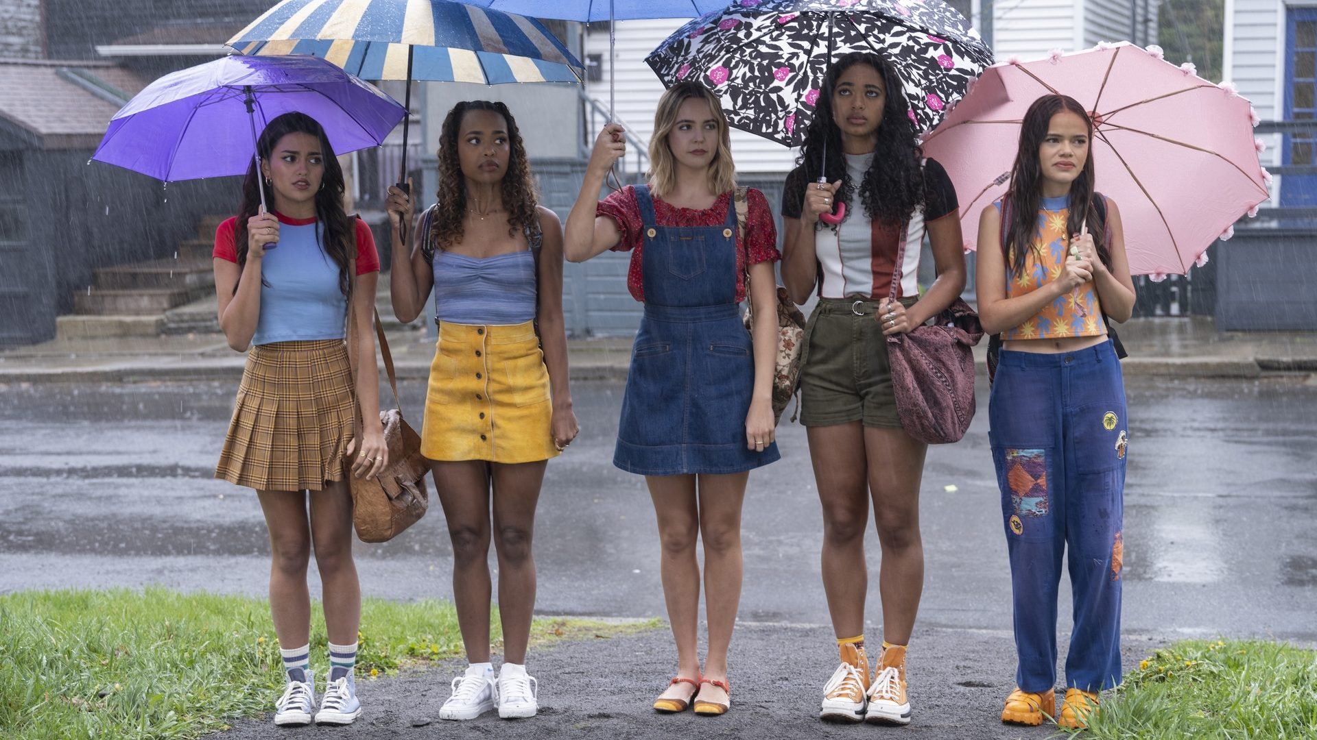 A group of five girls stand in a line on a rainy day, each of them holding a different umbrella