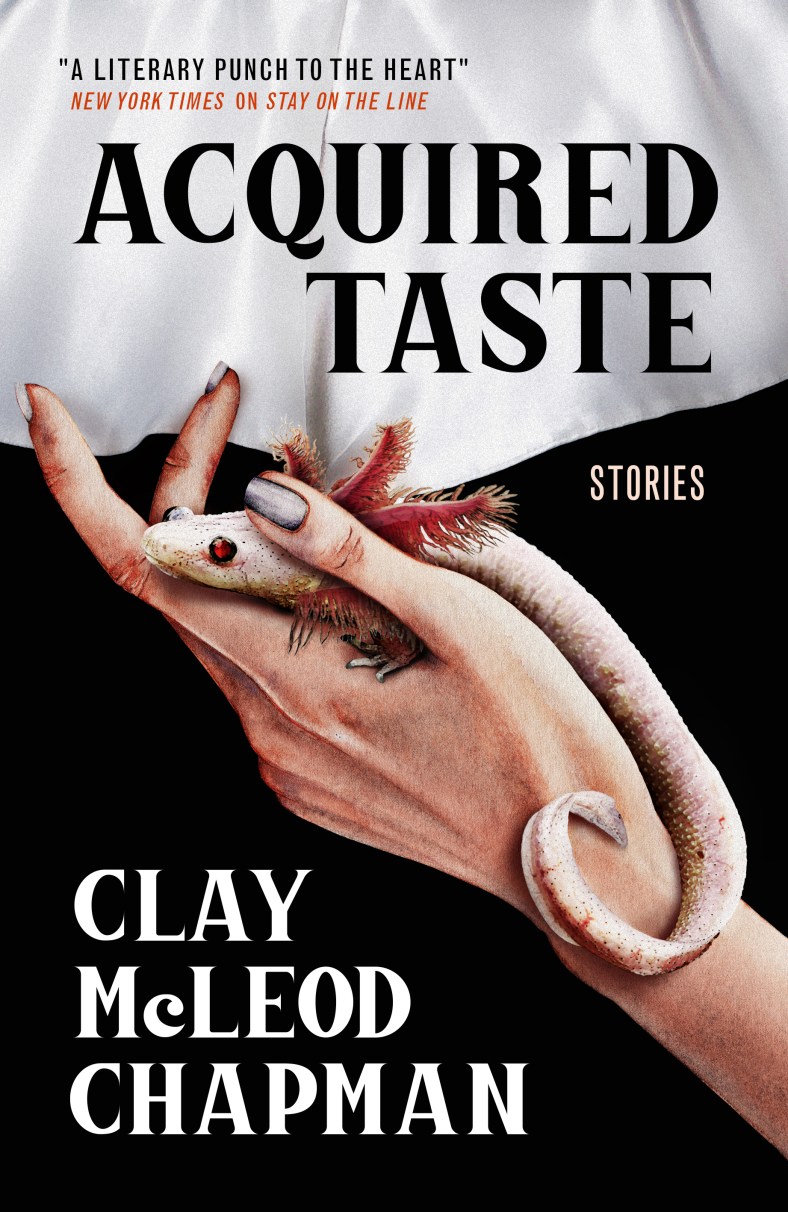 acquired taste cover featuring a hand with polished silver fingernails holding what looks like an axolotl. It's sent against a black bacakground with a white cloth on the top of the image.